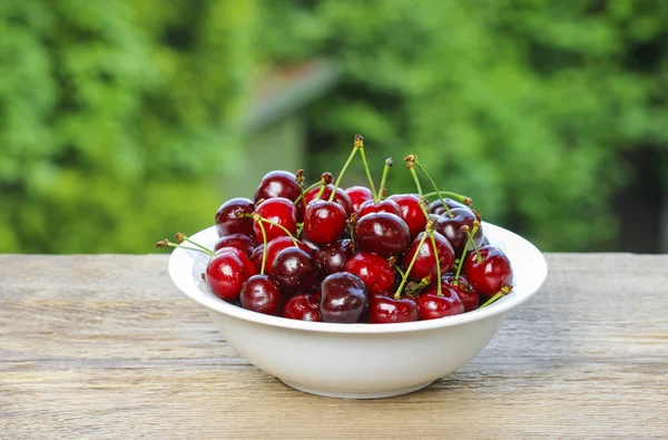 Fresh cherries in wicker basket on wooden table in the garden — Stock Photo, Image