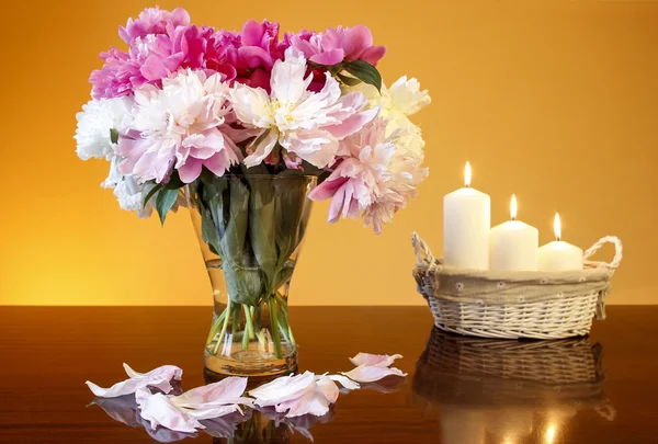 Buquê de peônias em vaso de vidro e cesta de velas — Fotografia de Stock