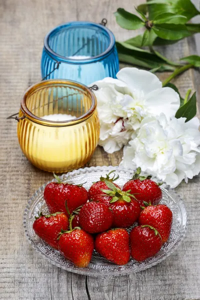 Aardbeien, kaarsen en witte pioenroos bloem op houten tafel — Stockfoto