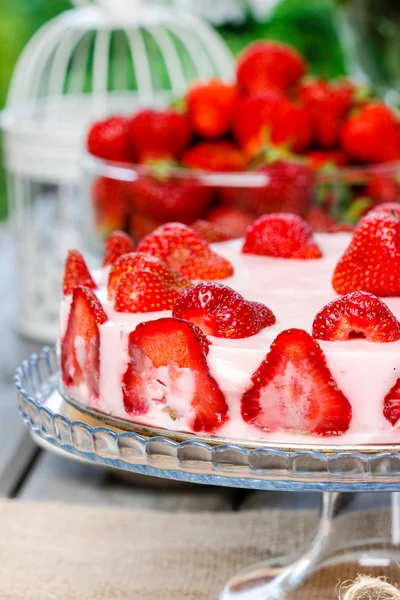 Strawberry cake on rustic wooden table in lush summer garden — Stock Photo, Image