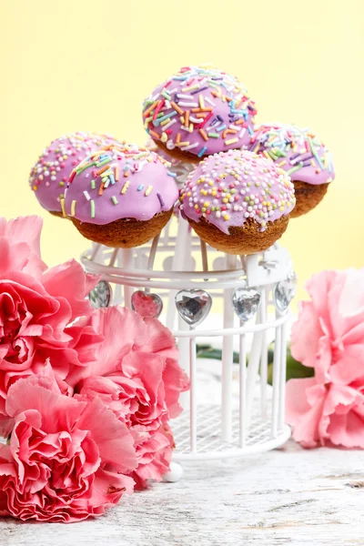 Cake Pops auf hölzernem Hintergrund zwischen Nelkenblüten — Stockfoto