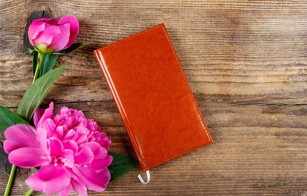 Kleines Buch und üppige rosa Pfingstrosen auf dem Holztisch. Ansicht von oben — Stockfoto