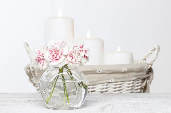 Boeket van roze anjers in kleine glazen vaas. witte kaarsen — Stockfoto