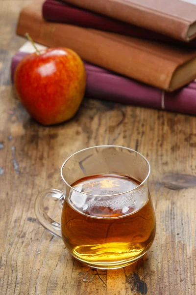 Un vaso de té caliente sobre una mesa de madera. Montón de libros — Foto de Stock