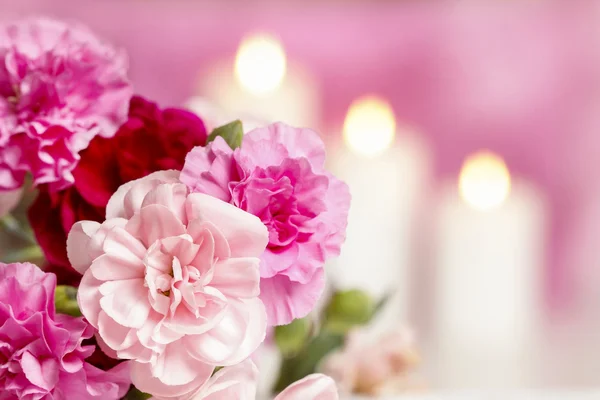 Boeket van carnation-roze bloemen. kaarsen op de achtergrond — Stockfoto