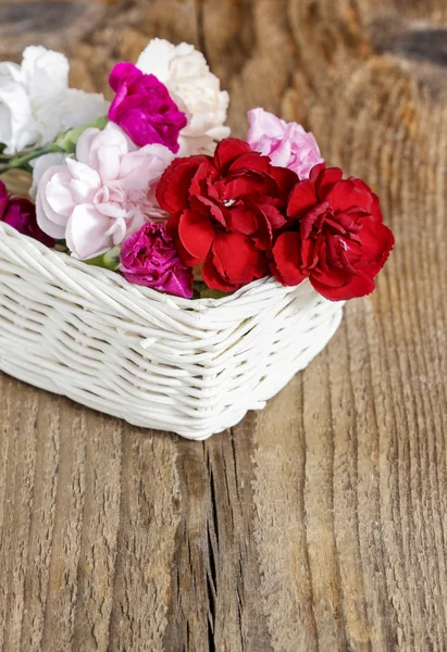 Rote, rosa und weiße Nelkenblüten im Weidenkorb auf Holz — Stockfoto