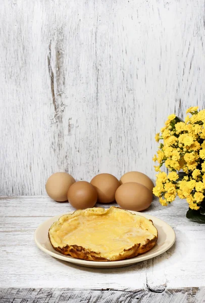 Tortilla sobre mesa de madera blanca, huevos en el fondo — Foto de Stock