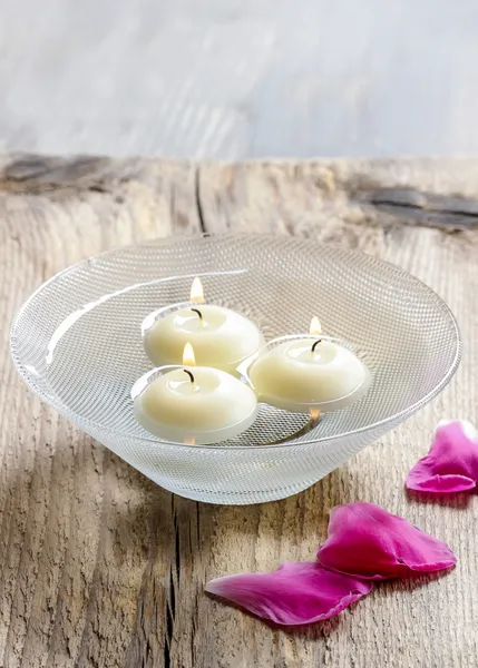 Zwevende kaarsen in water onder roze bloemblaadjes. Aromatherapie in spa — Stockfoto