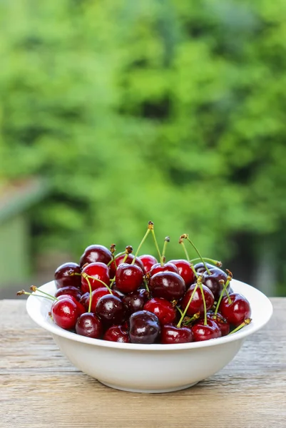 Friss cseresznye és meggy, fehér tálban, a kertben fából készült asztal — Stock Fotó