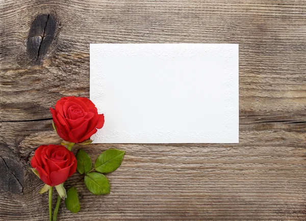 Rote Rosen auf hölzernem Hintergrund. leeres Blatt Papier. Kopierraum lizenzfreie Stockbilder