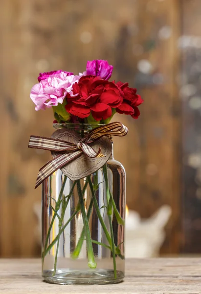 Färgglada nejlikor blommor i genomskinligt glasvas på trä b — Stockfoto