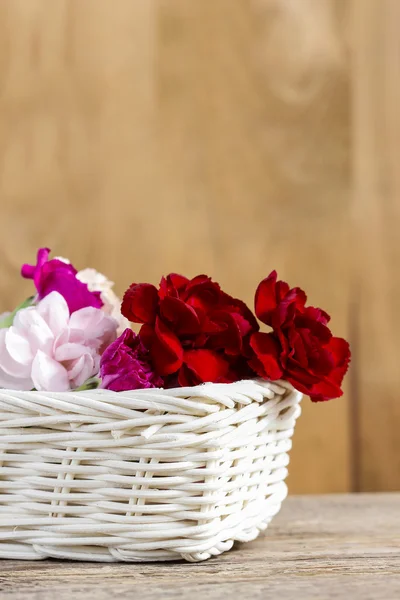 Rote, rosa und weiße Nelkenblüten im Weidenkorb auf Holz — Stockfoto