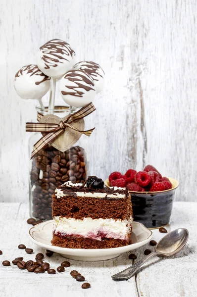 Chocolate and cherry cake on white plate. Cake pops in glass jar — Stock Photo, Image