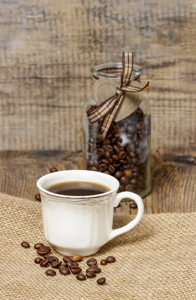 Tasse Kaffee auf hessischer Serviette. Kaffeebohnen herum. selektiv — Stockfoto