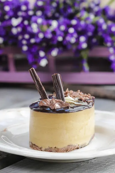 Cappuccino-Kuchen auf weißem Teller. lila Blumen im Hintergrund — Stockfoto