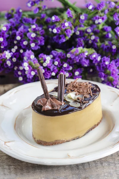 Cappuccino cake on white plate. Purple flowers in the background — Stock Photo, Image