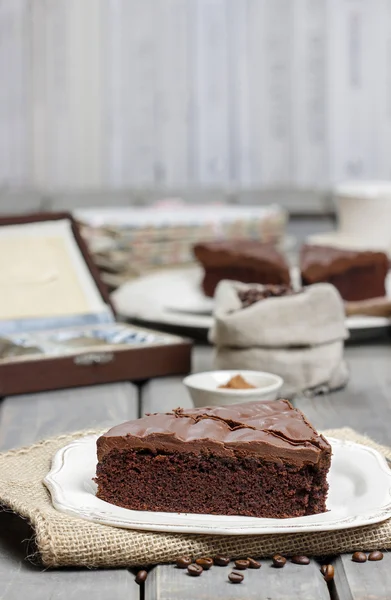 Pastel de chocolate en plato blanco, en hessian. Granos de café sobre madera —  Fotos de Stock