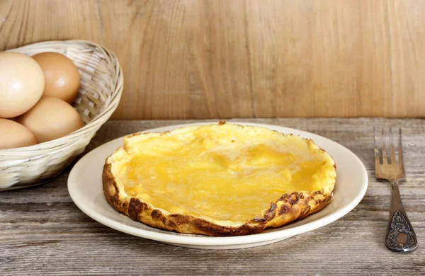 Omelette on wooden table. Basket with eggs in the background — Stock Photo, Image