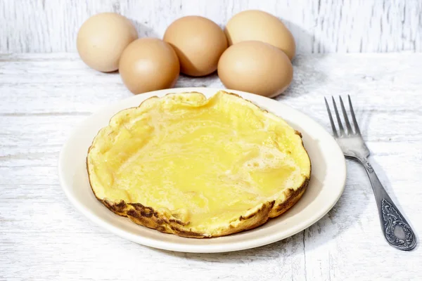 Tortilla sobre mesa de madera. Cesta con huevos en el fondo — Foto de Stock