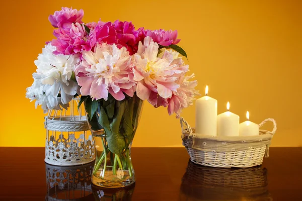 Bouquet di peonie in vaso di vetro e cesto di candele su legno — Foto Stock