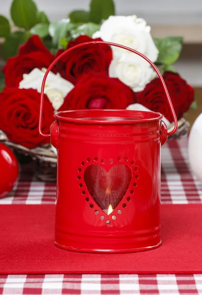 Red iron lantern with heart shape. Basket of roses in the backgr — Stock Photo, Image