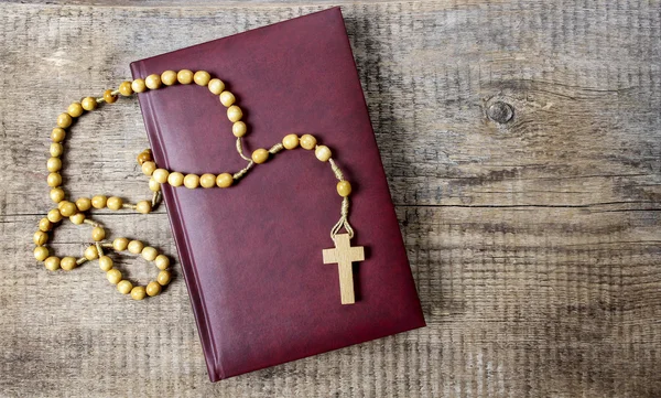 Holy Bible, rosary and red rose petals on wooden table. Copy spa — Stock Photo, Image