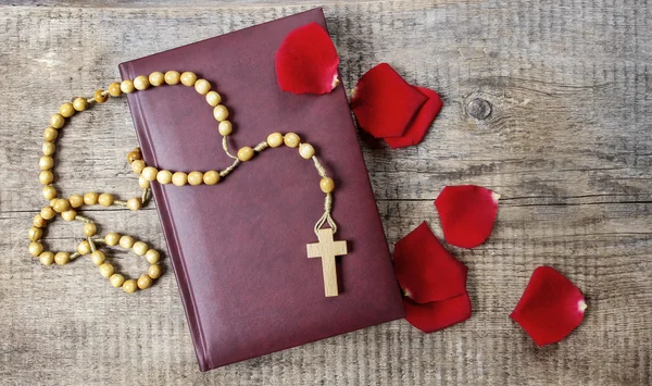 Heilige Bijbel, rozenkrans en rood roze bloemblaadjes op houten tafel. kopie spa — Stockfoto