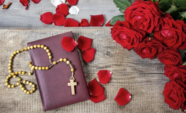 Santa Biblia, rosario y pétalos de rosa roja en la mesa de madera. Copiar spa — Foto de Stock