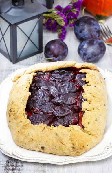 Plum galette on wooden table. Raw plums and pumpkins in the back — Stock Photo, Image