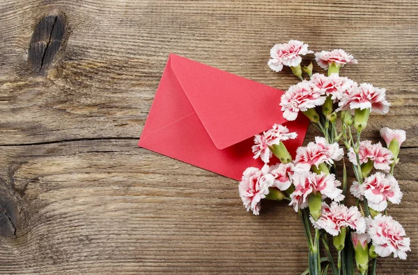 红色和白色的康乃馨和孤立在木头上的红信封 — 图库照片