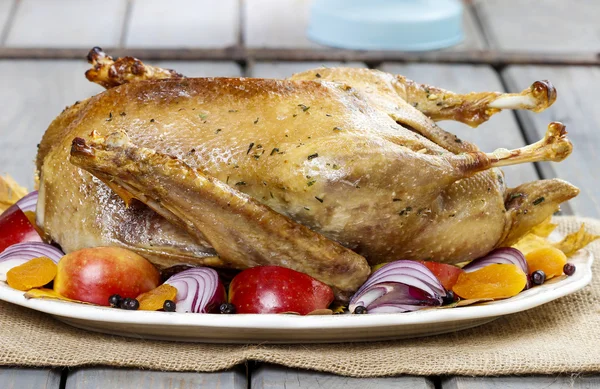 Roasted goose with apples and vegetables on wooden table. Stock Photo