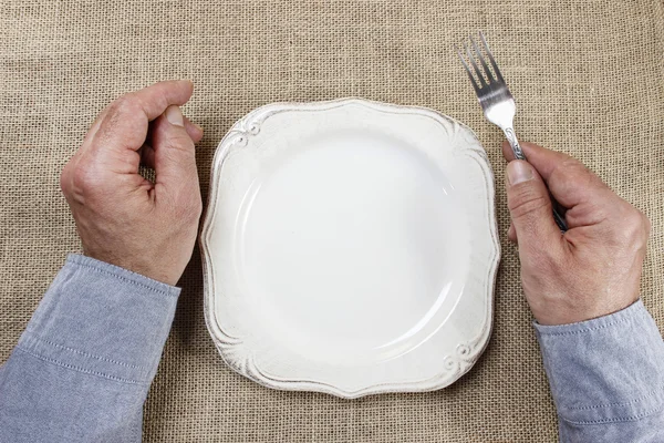 Голодный человек ждет свою еду за пустой тарелкой на столе — стоковое фото