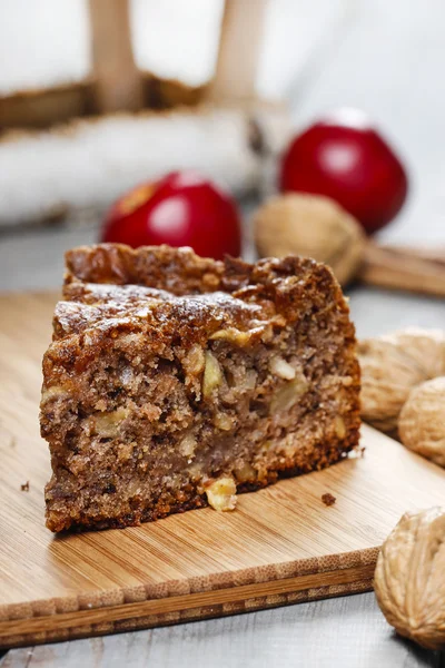Cinnamon cake on wooden tray. Red apples and nuts in the back — Stock Photo, Image