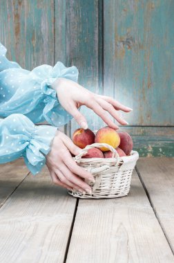 Woman choosing peaches from wicker basket