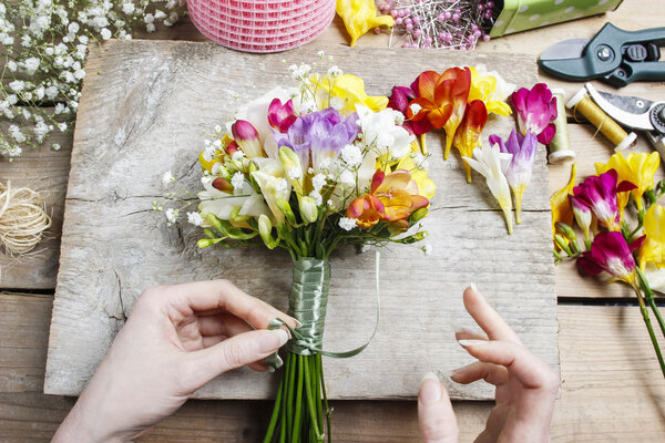 Флорист на работе. Женщина делает букет из цветов фрезии
