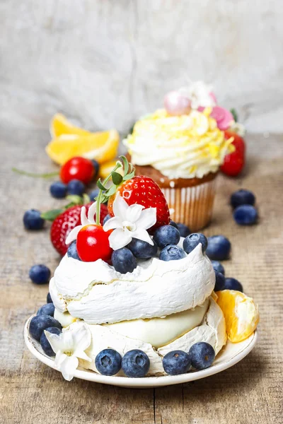 Meringue cake decorated with fresh fruits, standing on wooden ta — Stock Photo, Image