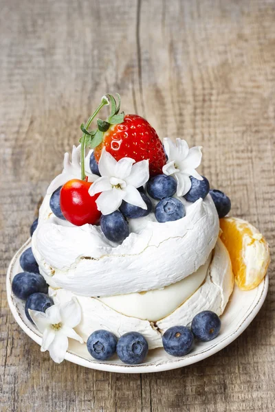 Meringue cake decorated with fresh fruits, standing on wooden ta — Stock Photo, Image