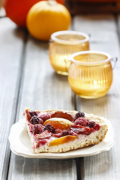 Piece of blueberry, peach and plum cake on rustic wooden table