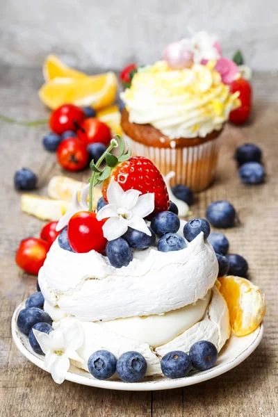 Meringue cake decorated with fresh fruits, standing on wooden ta — Stock Photo, Image