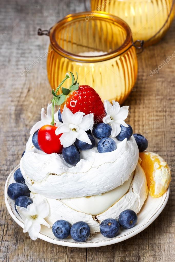 Meringue cake decorated with fresh fruits, standing on wooden ta