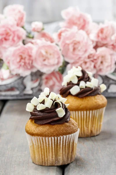Fancy chocolade cupcakes op houten tafel. Carnation roze bloemen — Stockfoto