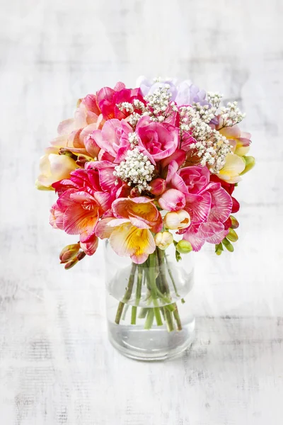 Bouquet of colorful freesia flowers in transparent glass vase. — Stock Photo, Image