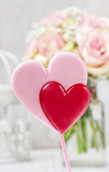 Lollipops in heart shape. Bouquet of pink roses in the backgroun — Stock Photo, Image