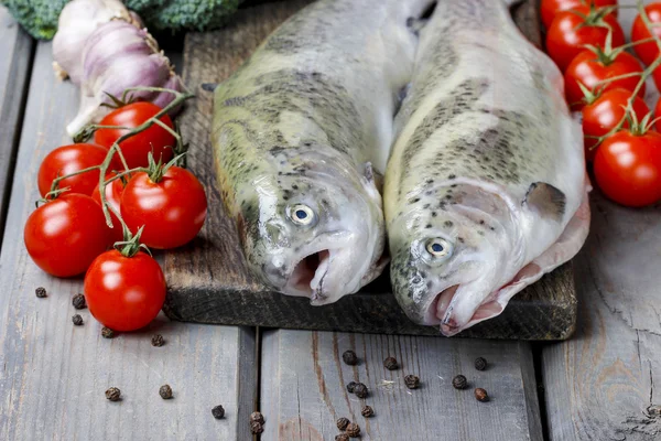 Due trote arcobaleno, pomodori e aglio sul tavolo rustico in legno — Foto Stock