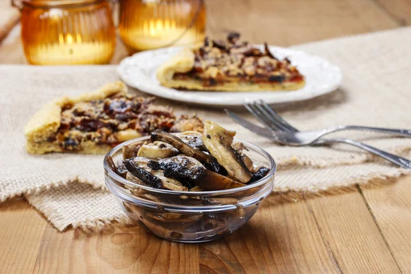 Bowl of raw mushrooms and mushroom galette in the background — Stock Photo, Image