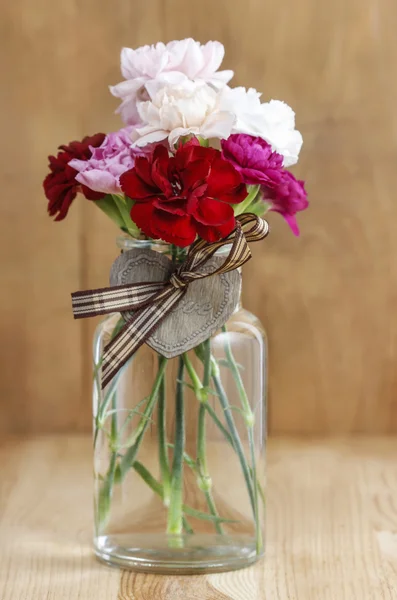 Färgglada nejlikor blommor i genomskinligt glasvas på trä b — Stockfoto