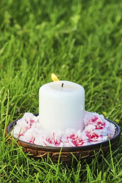 Vela blanca entre flores de clavel en cuenco de madera vintage —  Fotos de Stock