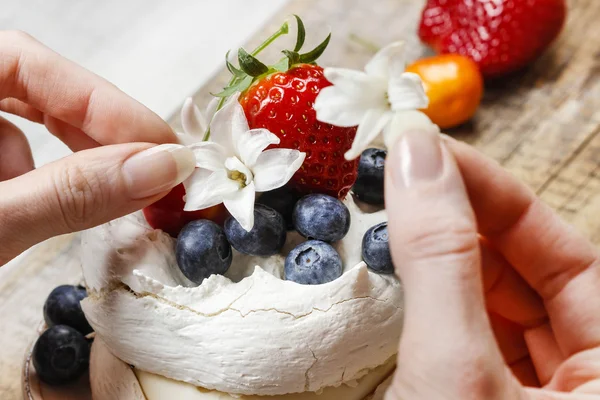 Женщина украшает торт безе съедобными цветами и свежими фрю — стоковое фото