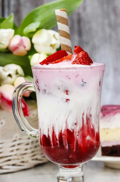 Erdbeer-Milchshake und ein Stück Kuchen im Hintergrund — Stockfoto