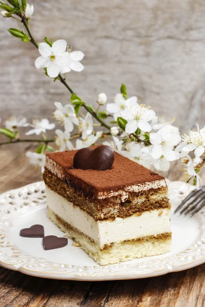Tiramisu cake on white plate. Blossom apple branch in the backgr — Stock Photo, Image